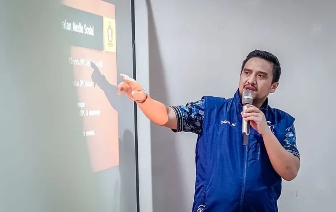 Thopaz berkemeja biru menyampaikan paparan sambil memegang mikrofon.